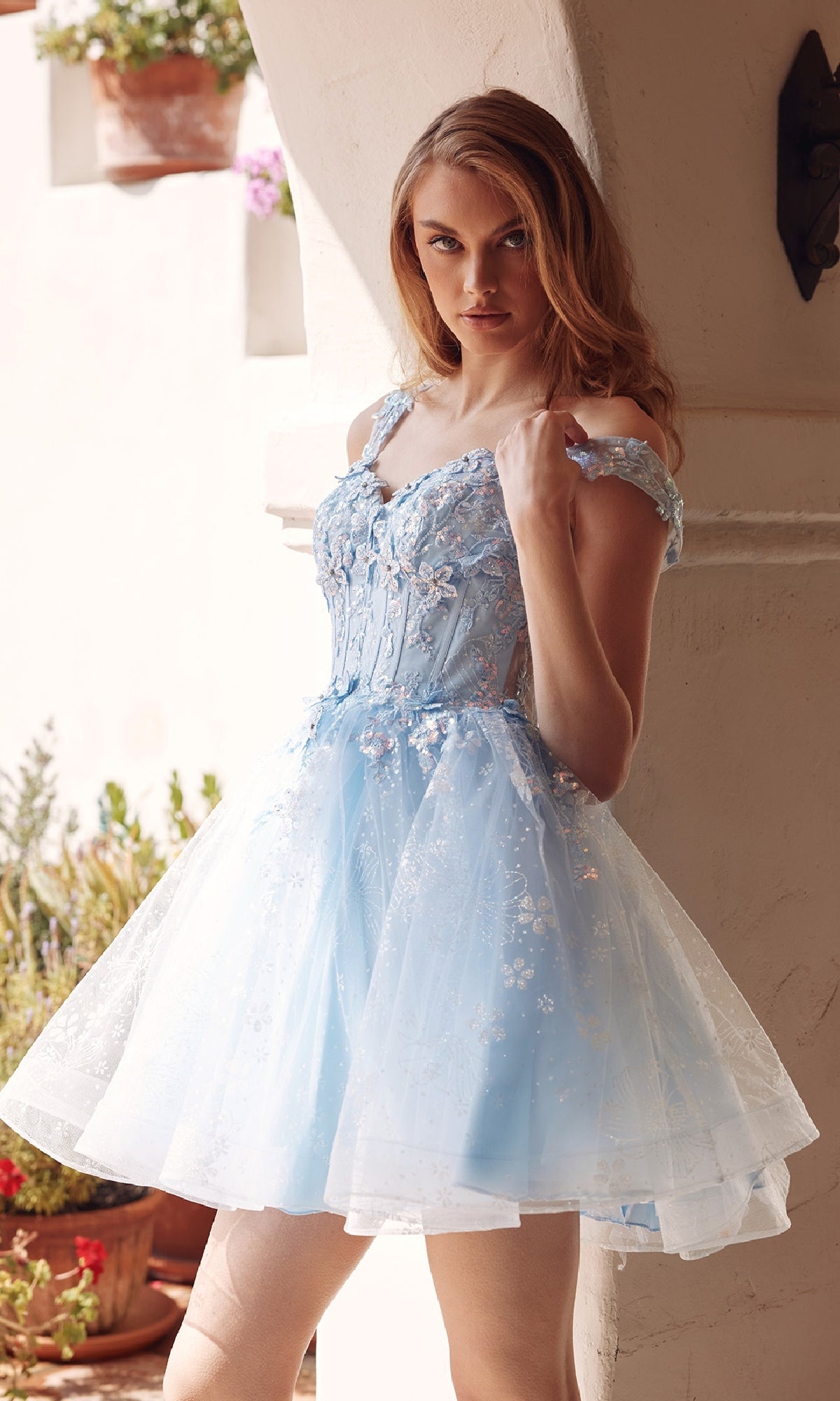 A woman wearing the Short Pastel A-Line Hoco Dress: Juliet JT976L, featuring embellished tulle, stands by a white archway and looks at the camera.